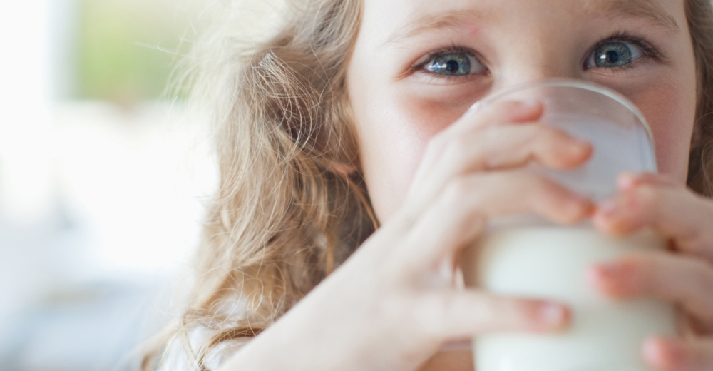 A little girl drinking milk from a glass tumbler.
