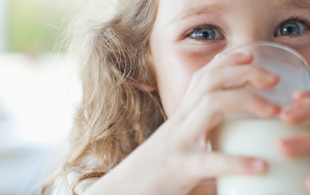 A little girl drinking milk from a glass tumbler.