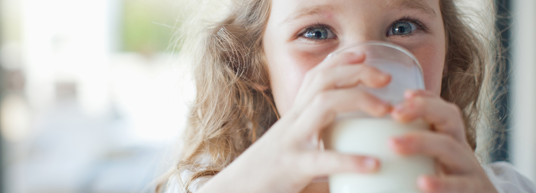 A little girl drinking milk from a glass tumbler.