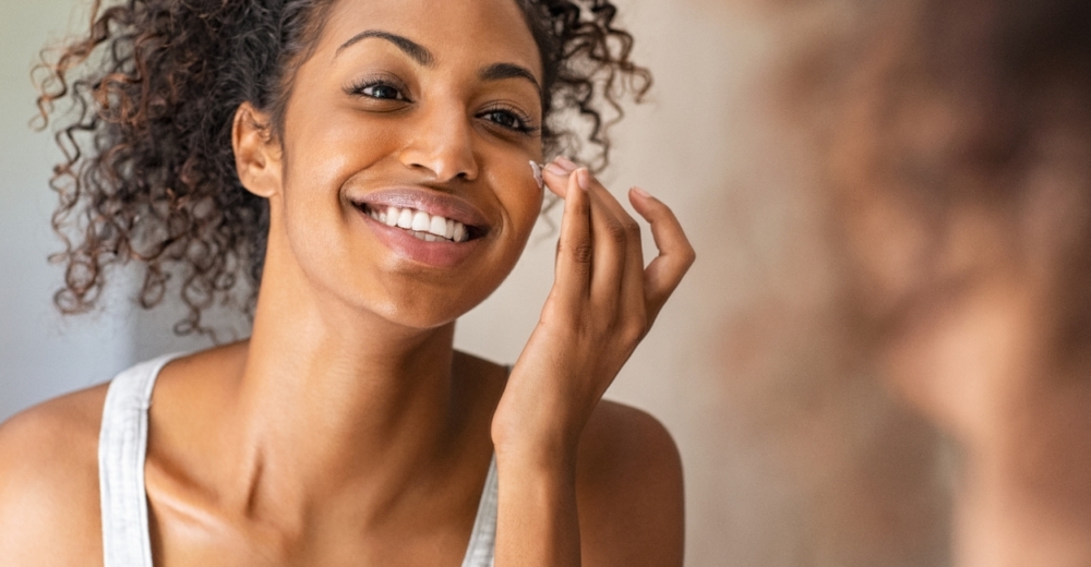 A girl applying cream to her face in front of a mirror