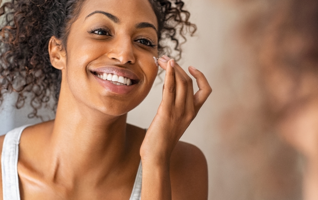 A girl applying cream to her face in front of a mirror