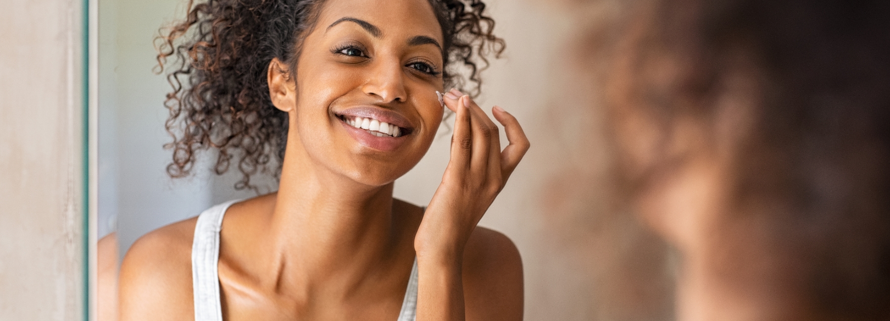 A girl applying cream to her face in front of a mirror