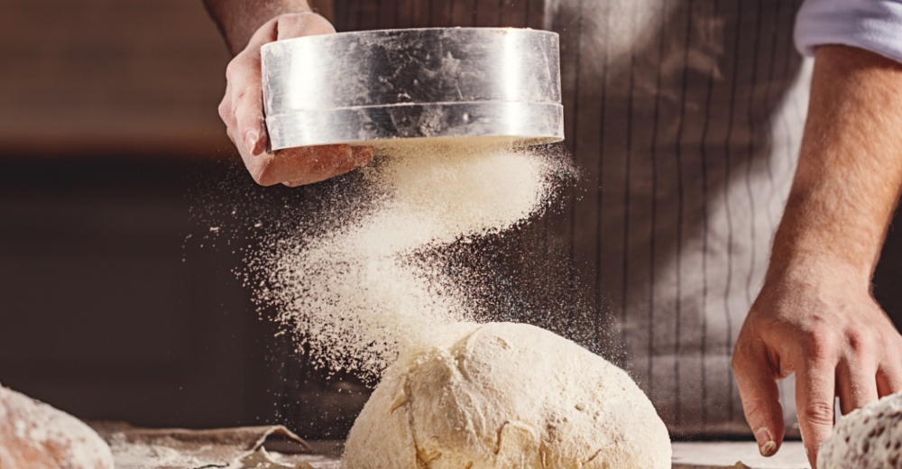 A baker pouring flour on a loaf of bread after baking.