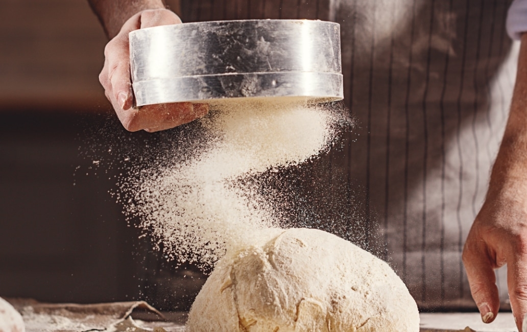A baker pouring flour on a loaf of bread after baking.