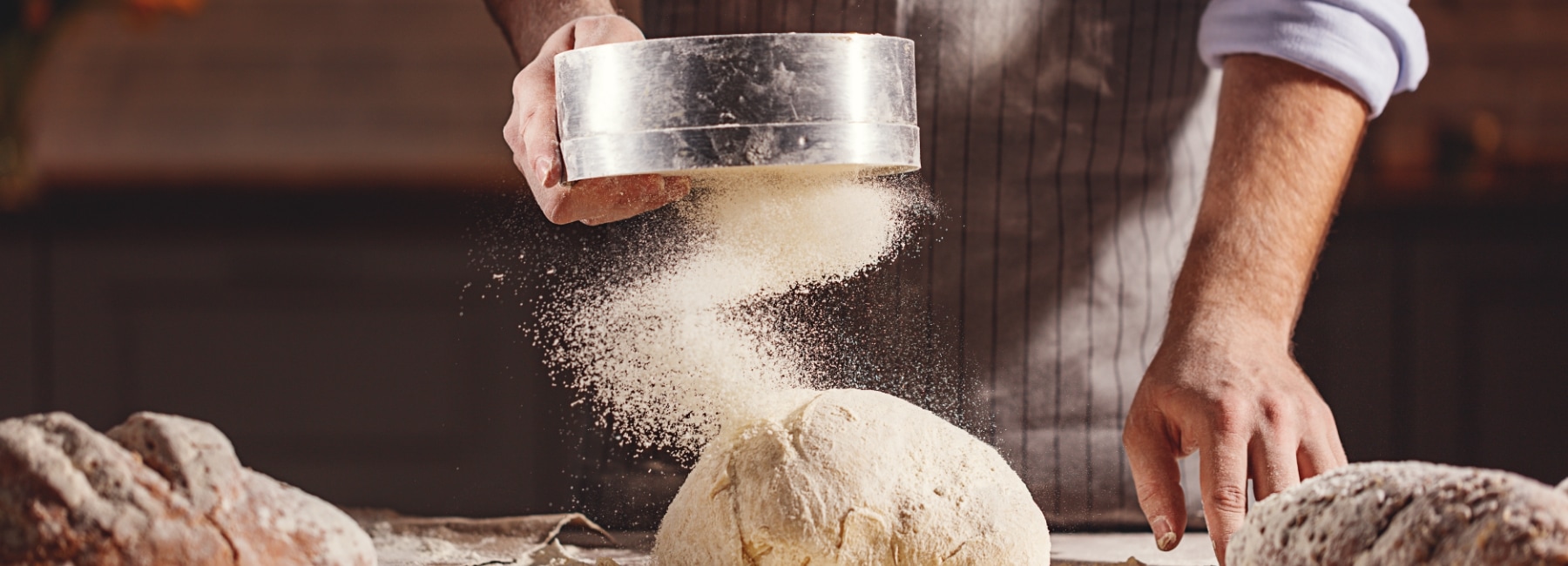 A baker pouring flour on a loaf of bread after baking.