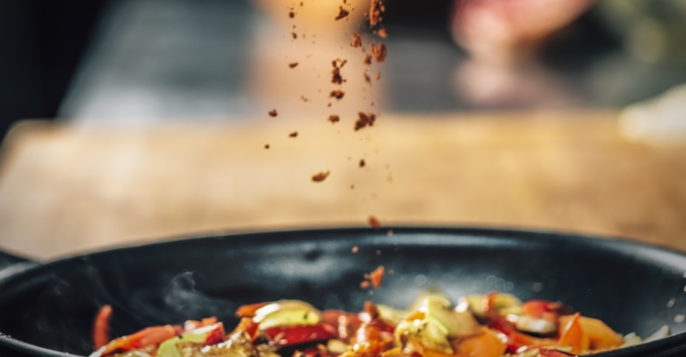 A frying pan with food where condiments are being poured.