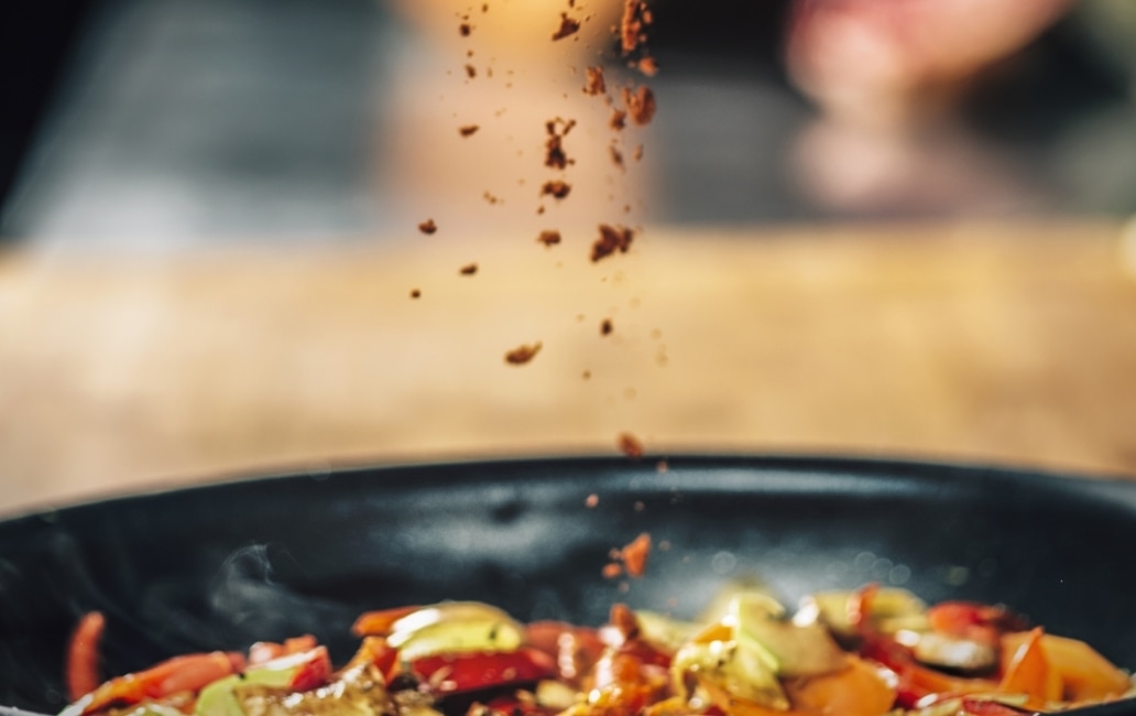 A frying pan with food where condiments are being poured.