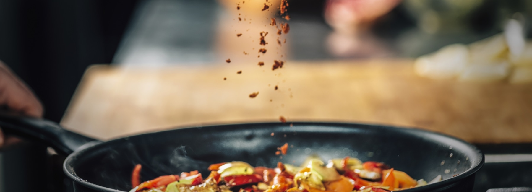 A frying pan with food where condiments are being poured.