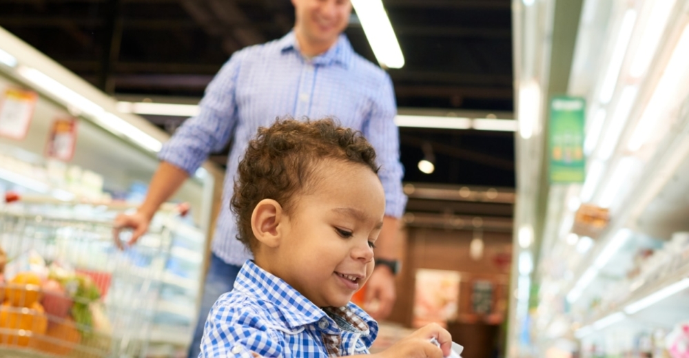 A child taking a container of yougurt from a supermarket fridge.