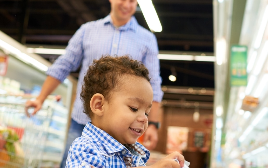 A child taking a container of yougurt from a supermarket fridge.