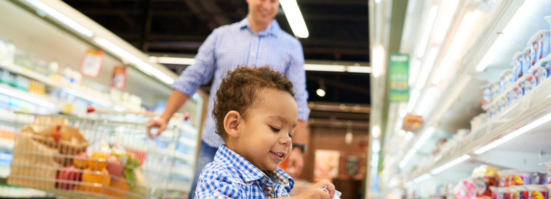 A child taking a container of yougurt from a supermarket fridge.