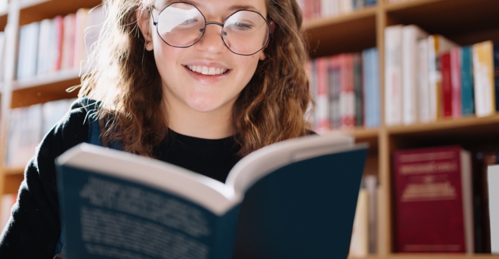 A person in a library smiling while reading a book.