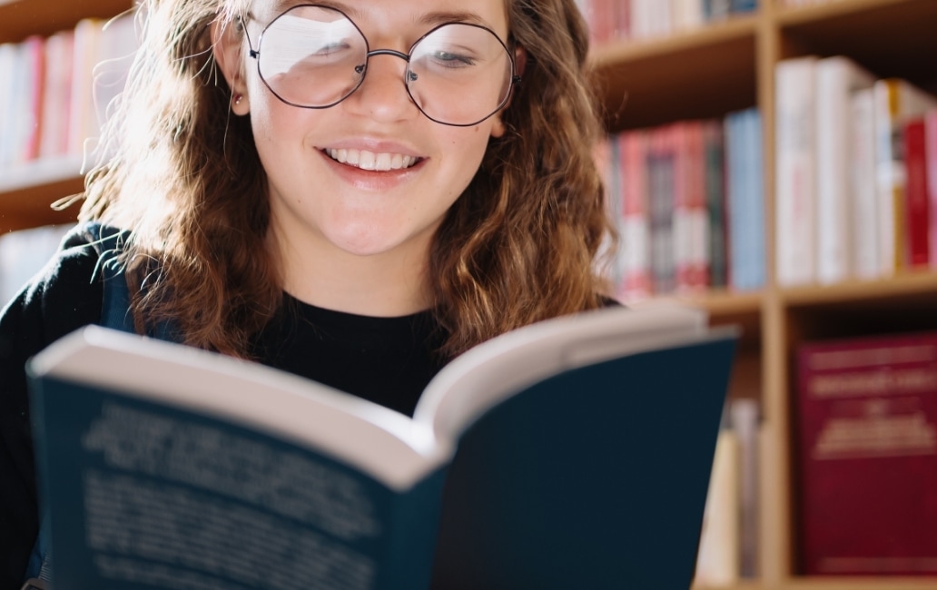 A person in a library smiling while reading a book.