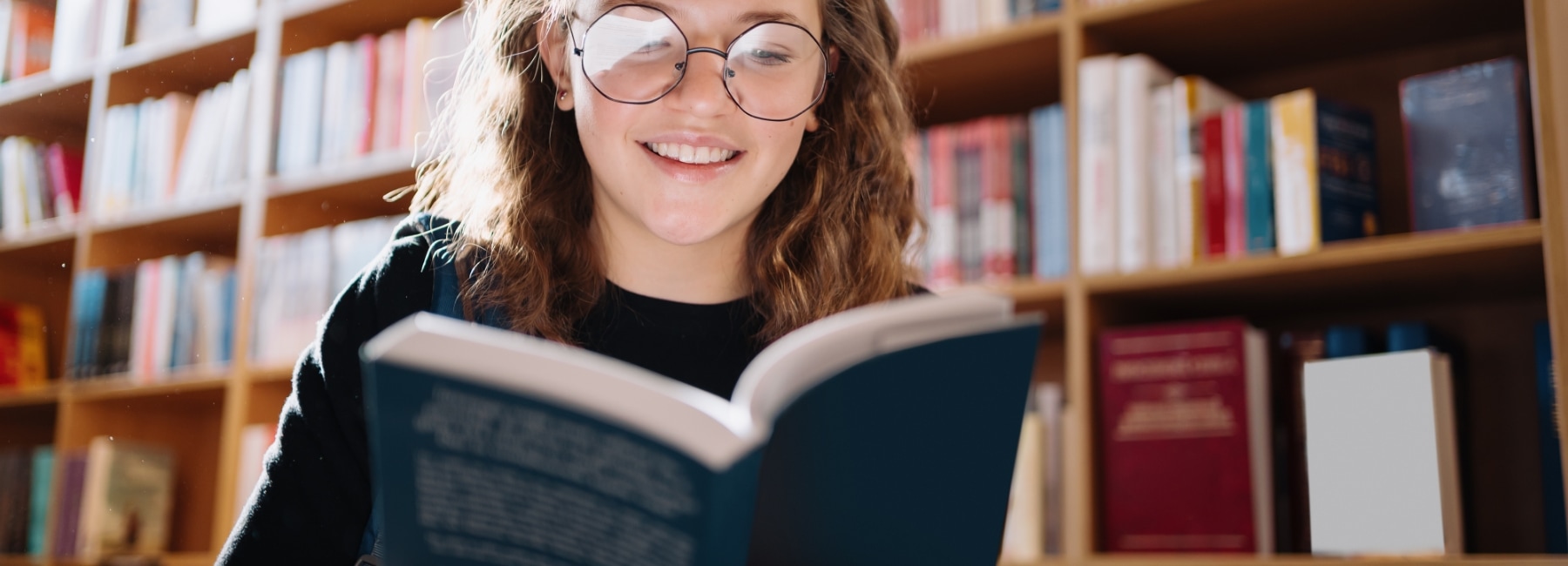 A person in a library smiling while reading a book.