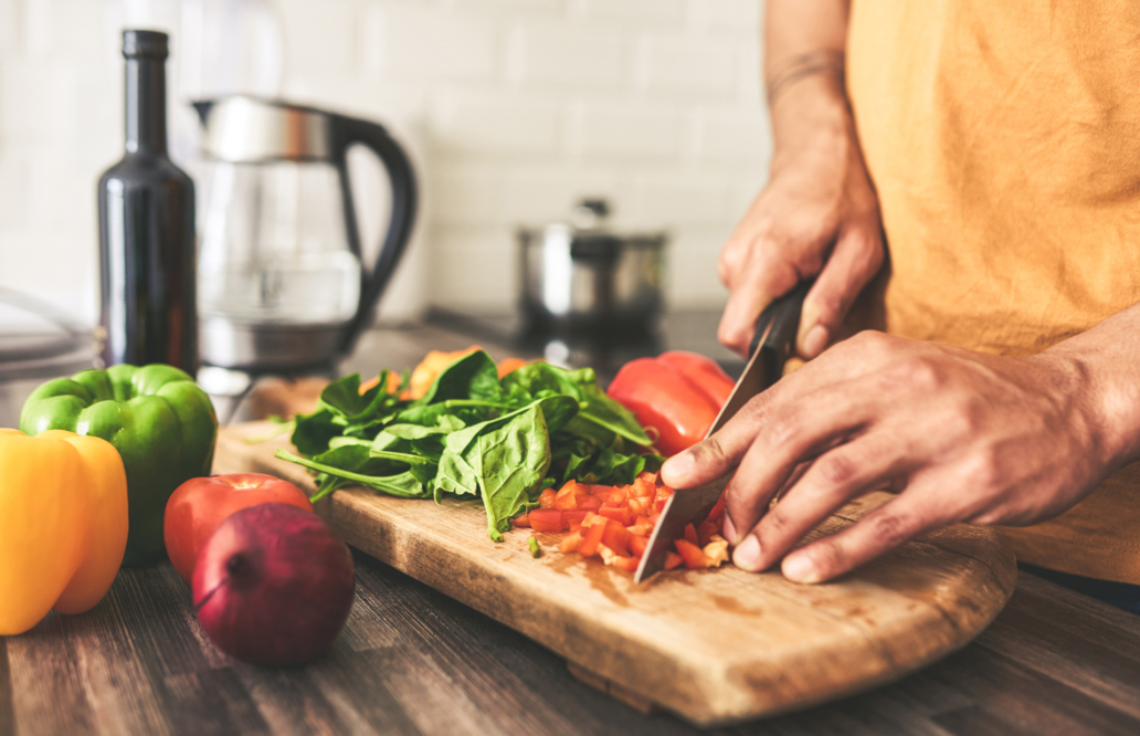 A man skillfully cuts fresh vegetables on a wooden cutting board in a well-lit kitchen setting.