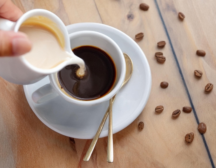 A hand is seen pouring freshly brewed coffee into a cup, set against the backdrop of a charming wooden table.